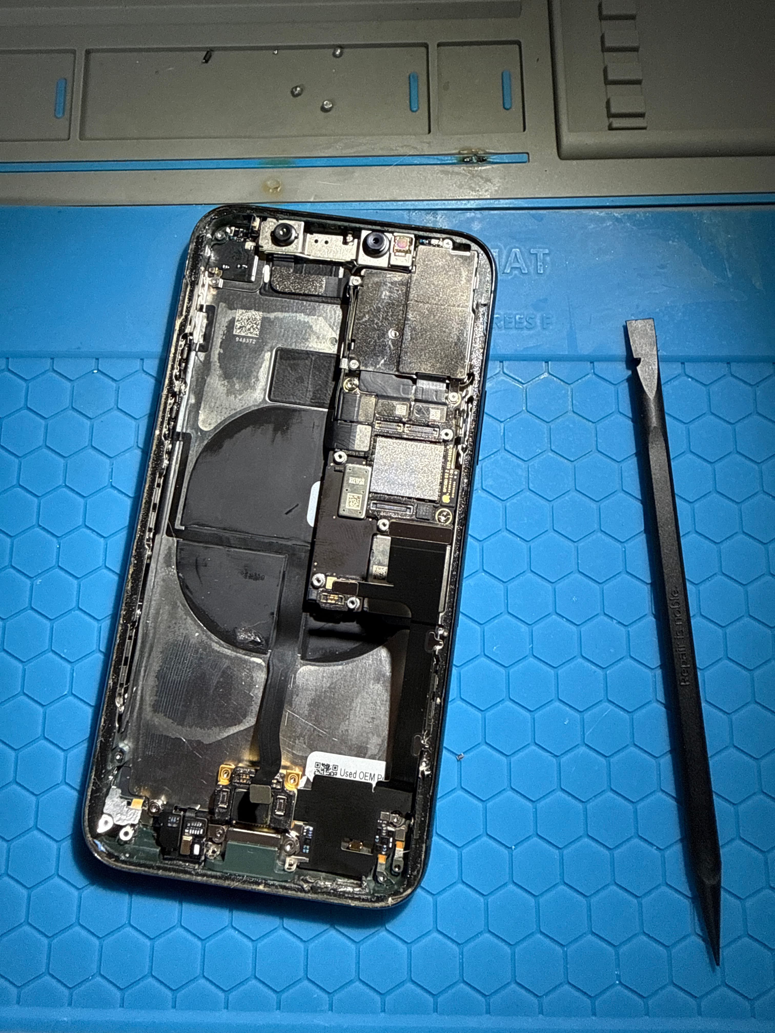 Disassembled smartphone showing internal components on a blue repair mat with a pry tool.