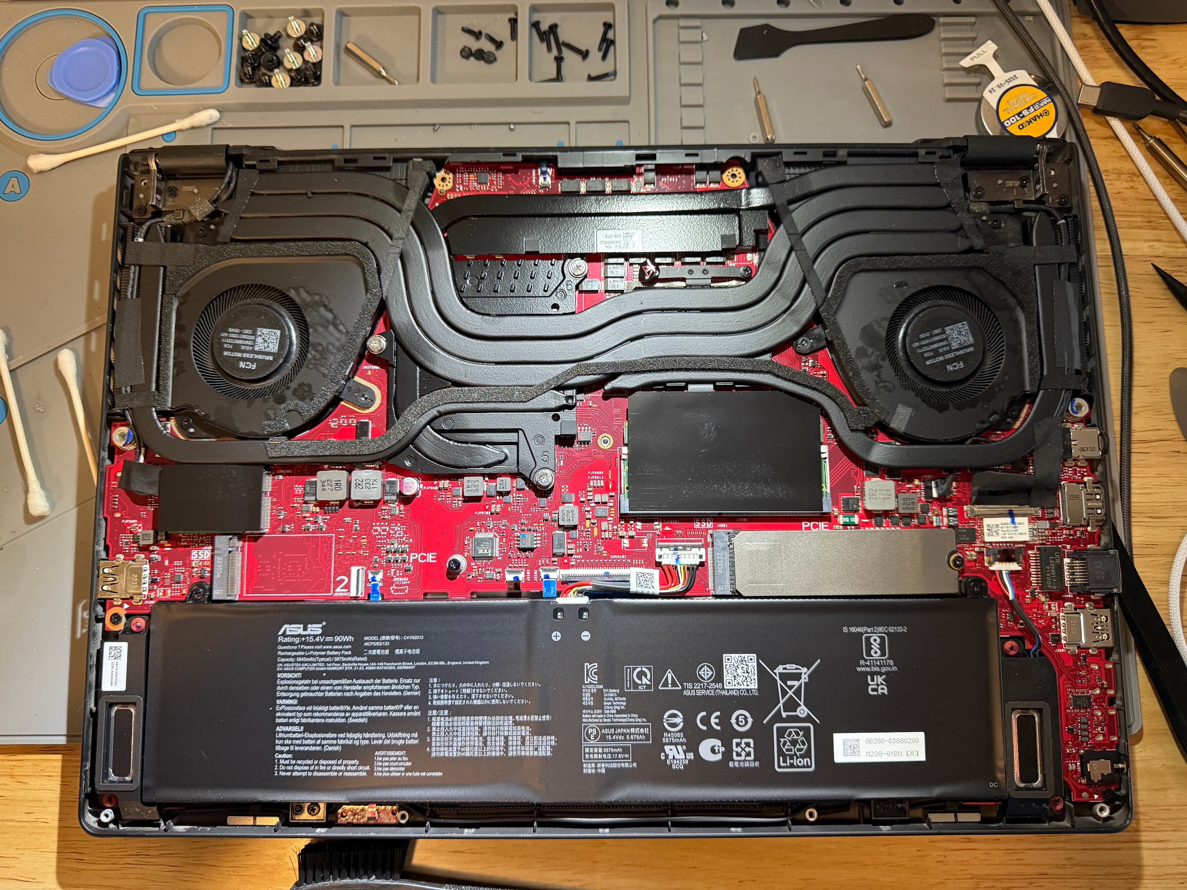 Open ASUS laptop revealing red motherboard, dual cooling fans, heat pipes, and large battery.
