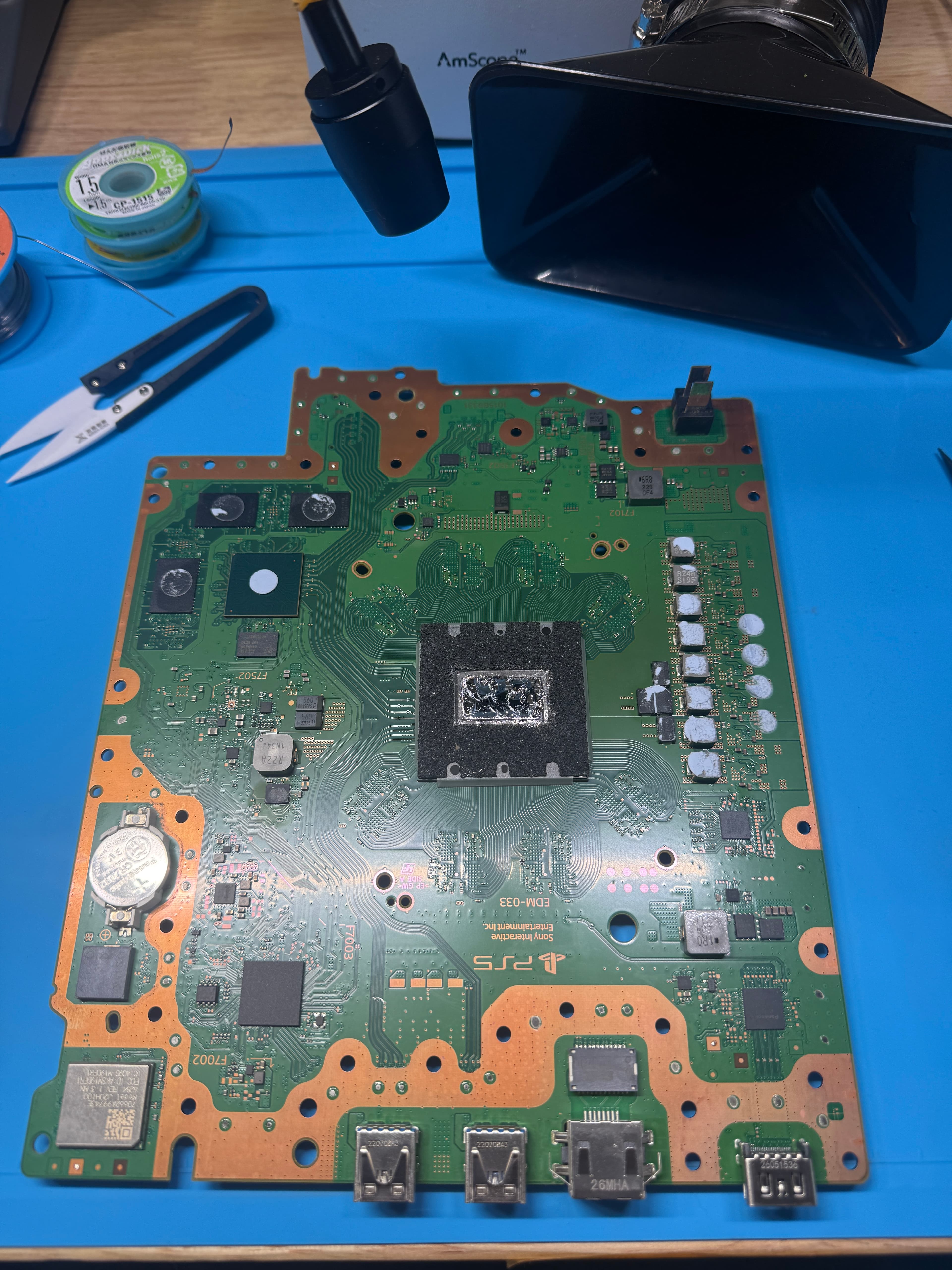 PlayStation 5 motherboard on a blue repair mat, showing the central processor and electronic components.