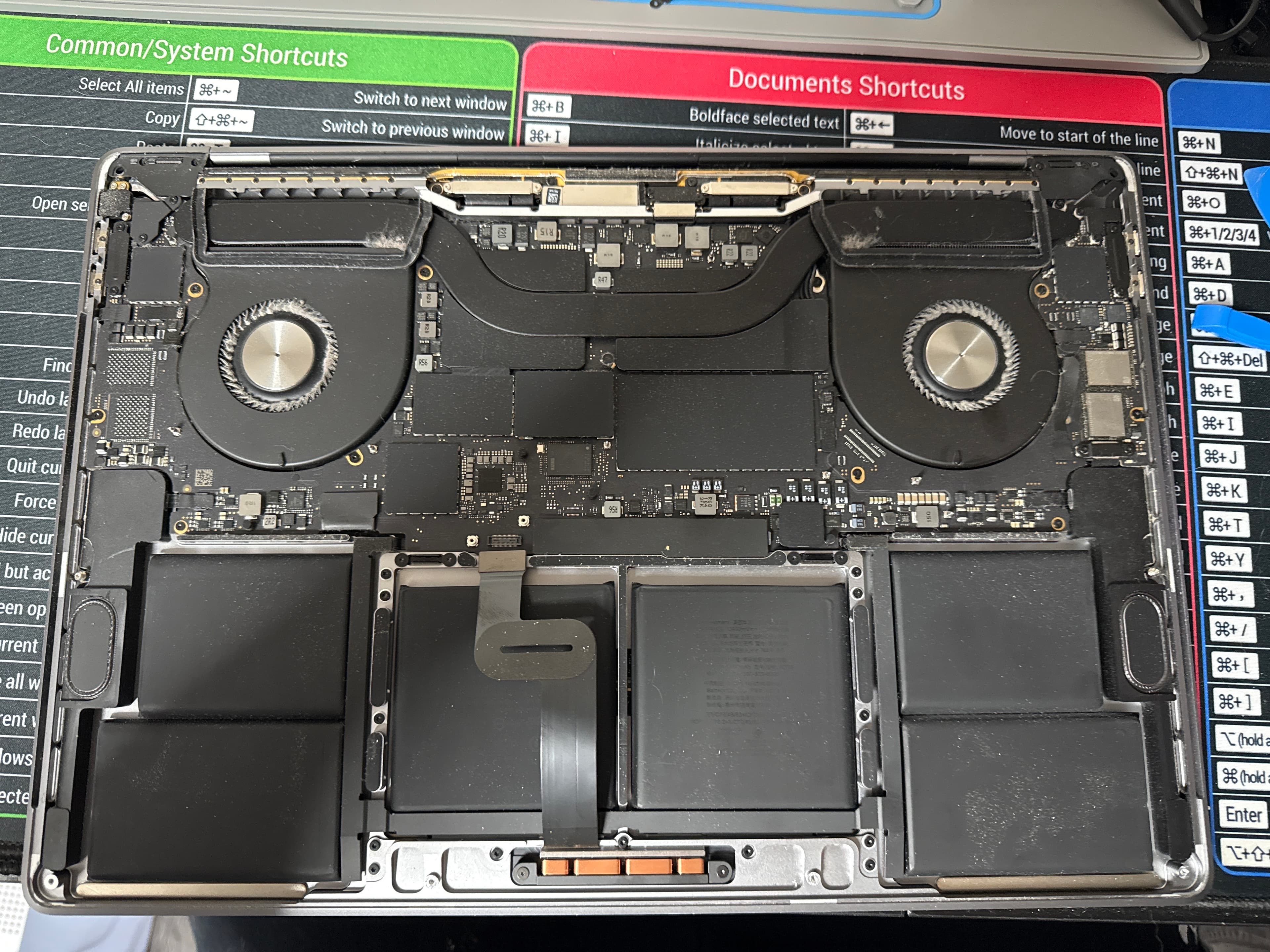 Internal view of an open laptop revealing dual cooling fans, logic board, and battery packs.